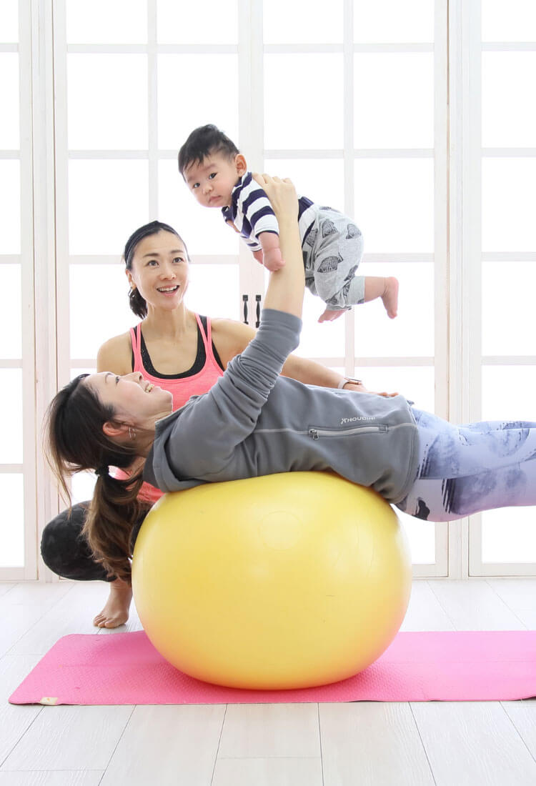 赤ちゃんを抱っこしながらバランスボールトレーニングをしている写真